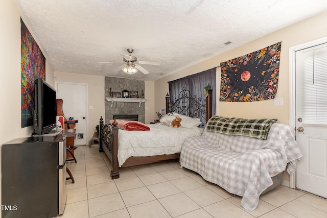 bedroom with visible vents, light tile patterned floors, a stone fireplace, a textured ceiling, and a ceiling fan