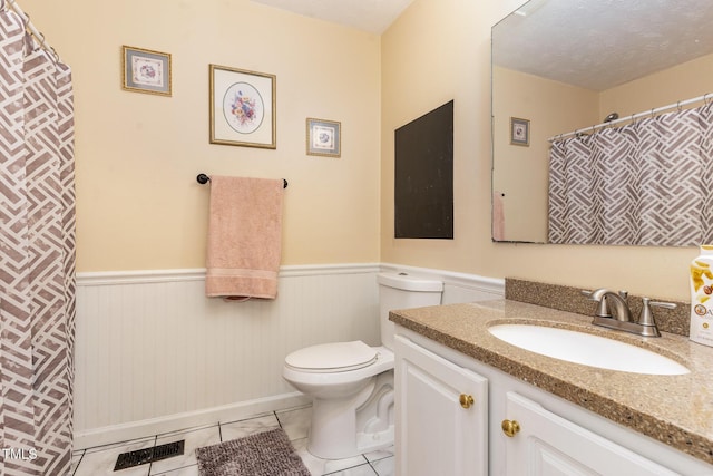 bathroom with tile patterned flooring, wainscoting, a textured ceiling, and toilet