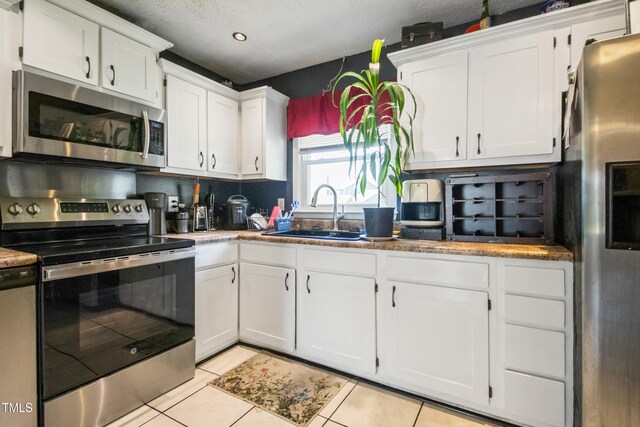 kitchen with recessed lighting, white cabinets, a sink, appliances with stainless steel finishes, and light tile patterned floors