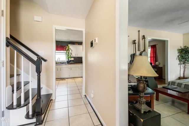 hallway with light tile patterned floors, baseboards, a sink, and stairway