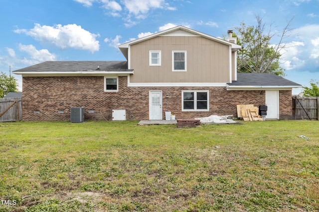 rear view of property with a chimney, central AC unit, brick siding, a fenced backyard, and a yard