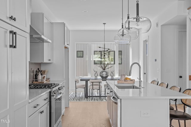 kitchen with a sink, a kitchen breakfast bar, stainless steel appliances, light wood finished floors, and light countertops