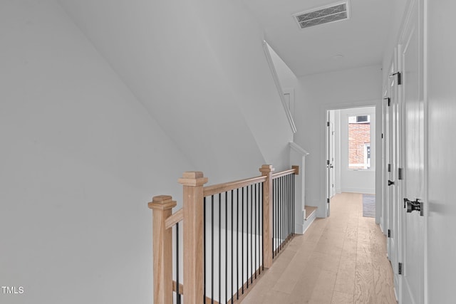 hallway with visible vents, an upstairs landing, and light wood finished floors