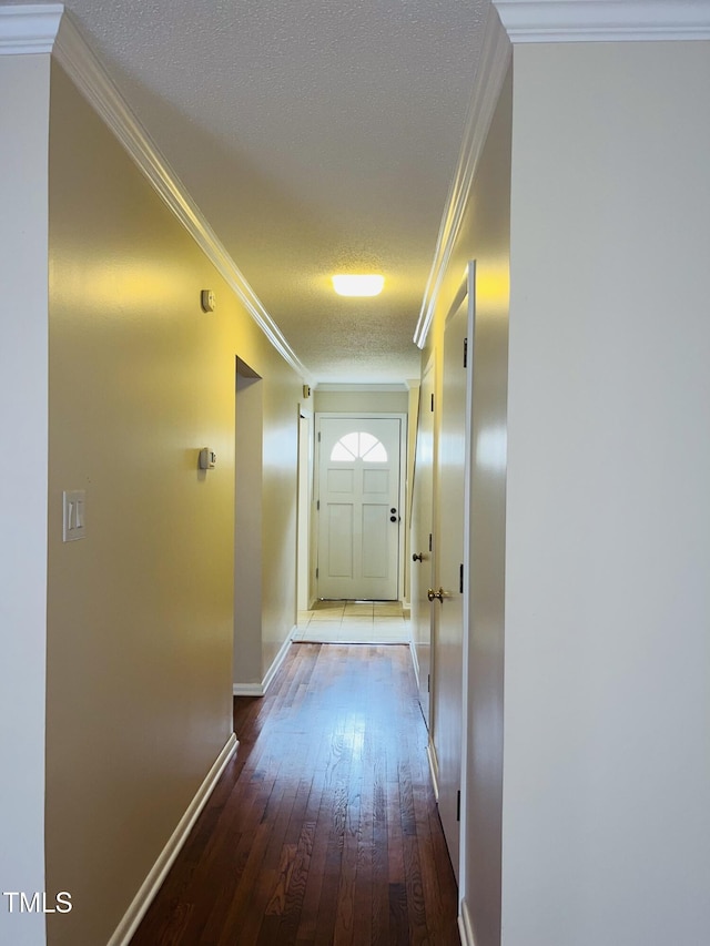 corridor with a textured ceiling, hardwood / wood-style flooring, baseboards, and ornamental molding