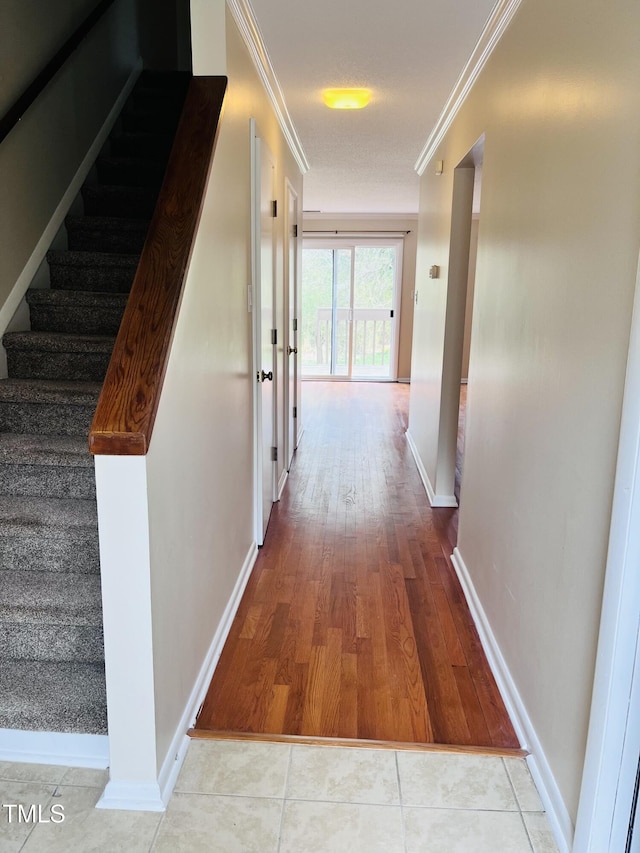 corridor with stairway, baseboards, crown molding, and tile patterned flooring