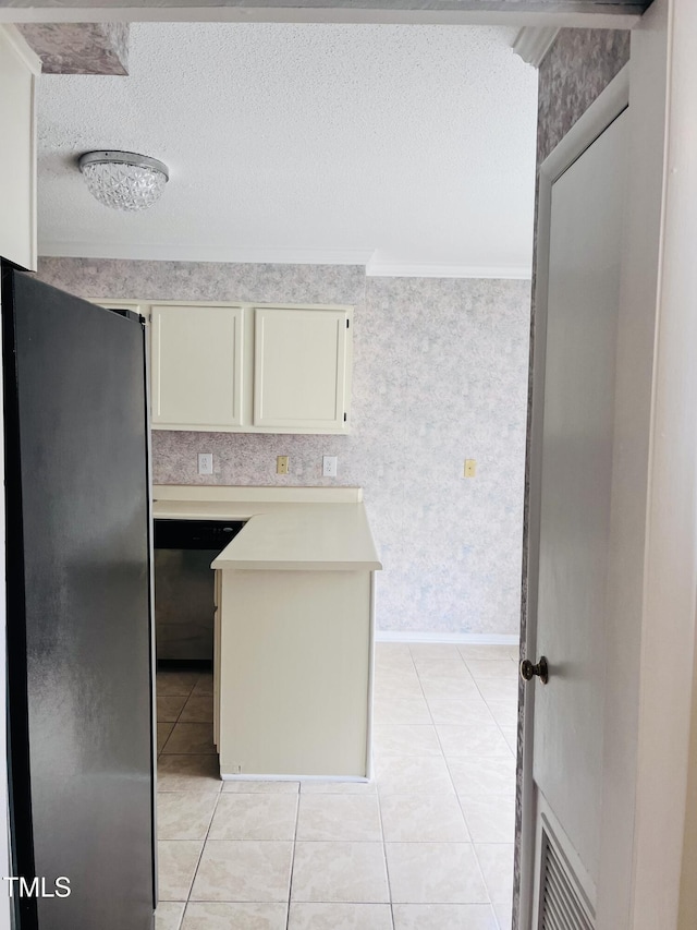 kitchen featuring a textured ceiling, stainless steel dishwasher, cream cabinets, freestanding refrigerator, and light countertops