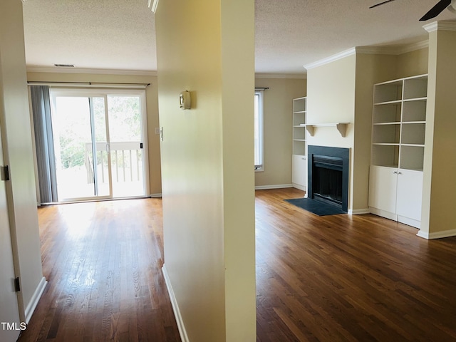 interior space with a textured ceiling, wood finished floors, baseboards, and ornamental molding