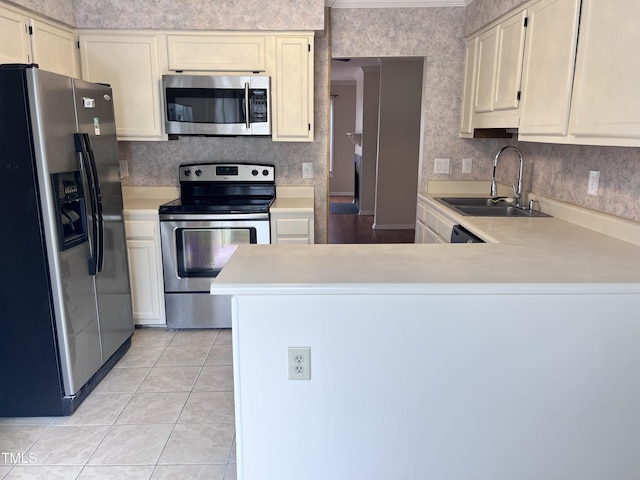 kitchen with appliances with stainless steel finishes, wallpapered walls, light countertops, and a sink