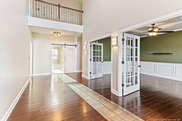 hallway with french doors, a high ceiling, a barn door, and wood-type flooring