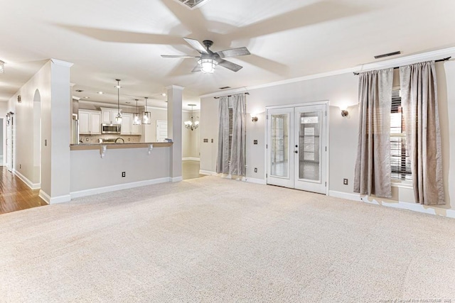 unfurnished living room featuring baseboards, ceiling fan with notable chandelier, visible vents, and light carpet