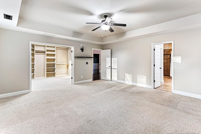 unfurnished bedroom featuring visible vents, a tray ceiling, baseboards, light colored carpet, and a spacious closet