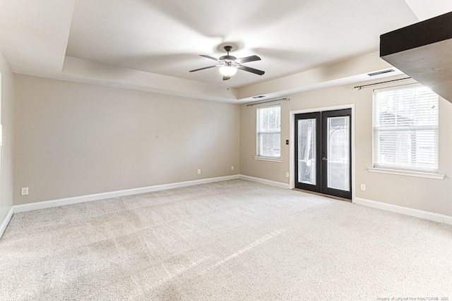 carpeted empty room with visible vents, baseboards, a tray ceiling, french doors, and a ceiling fan