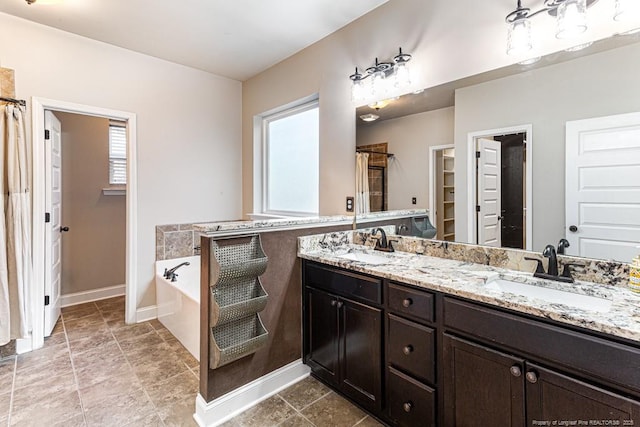 full bath with double vanity, baseboards, a garden tub, and a sink