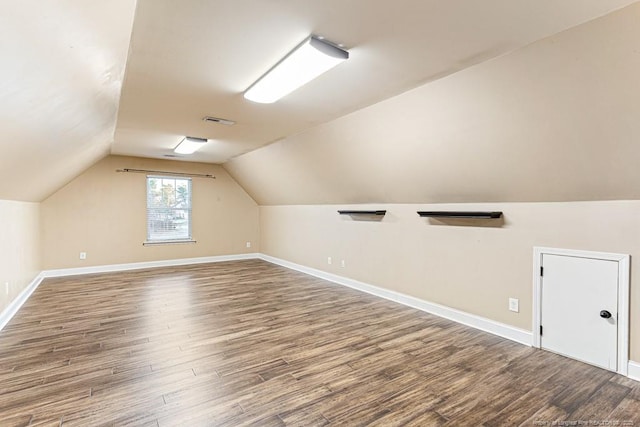 additional living space with vaulted ceiling, wood finished floors, baseboards, and visible vents