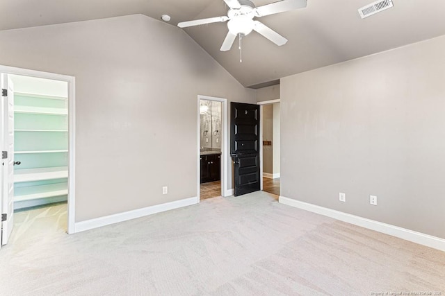 unfurnished bedroom with visible vents, light carpet, a walk in closet, lofted ceiling, and baseboards