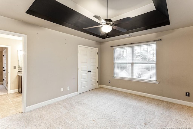 unfurnished bedroom with a tray ceiling, visible vents, baseboards, and light carpet