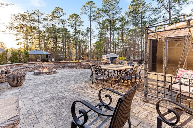 view of patio / terrace featuring an outbuilding, outdoor dining space, a fire pit, and a storage shed