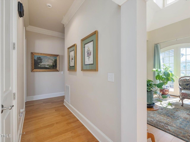 hall featuring light wood finished floors, visible vents, baseboards, and ornamental molding