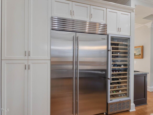 kitchen featuring light stone countertops, stainless steel built in fridge, ornamental molding, light wood-style flooring, and white cabinetry