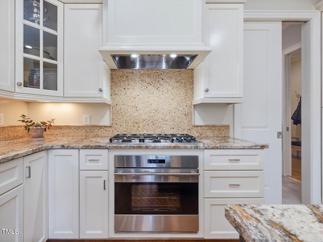 kitchen with glass insert cabinets, appliances with stainless steel finishes, decorative backsplash, and white cabinetry