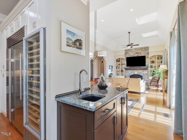 kitchen featuring light stone counters, built in shelves, light wood finished floors, a sink, and a stone fireplace