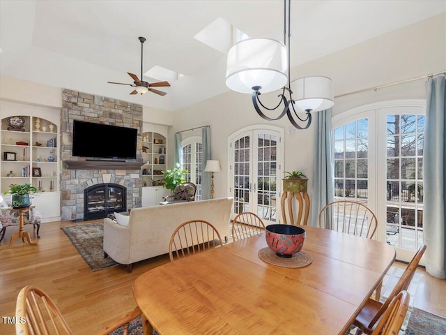 dining room featuring built in shelves, wood finished floors, ceiling fan, a stone fireplace, and french doors