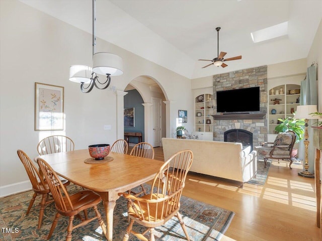 dining room with built in features, a ceiling fan, a fireplace, arched walkways, and light wood-style floors