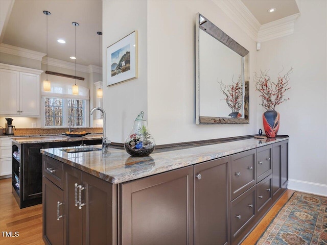 kitchen with light wood finished floors, crown molding, an island with sink, light stone counters, and white cabinets