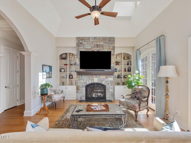 living area with built in shelves, ceiling fan, a fireplace, wood finished floors, and arched walkways