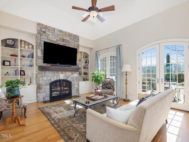 living area with built in shelves, a ceiling fan, wood finished floors, french doors, and a fireplace