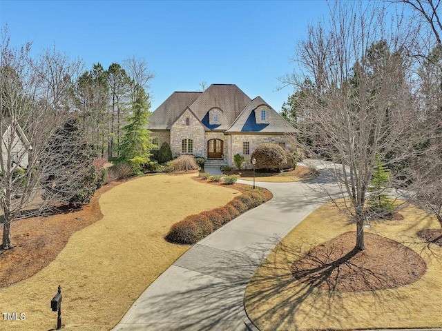 french provincial home featuring concrete driveway and stone siding