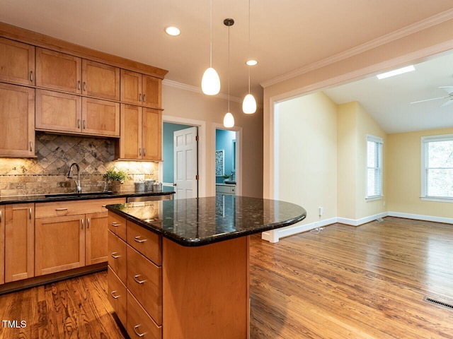 kitchen with a sink, tasteful backsplash, a kitchen island, wood finished floors, and crown molding