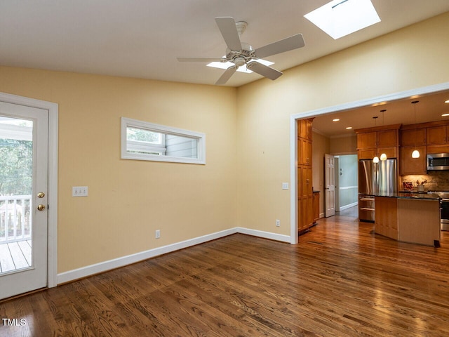 unfurnished living room featuring a ceiling fan, a skylight, baseboards, and dark wood-style flooring