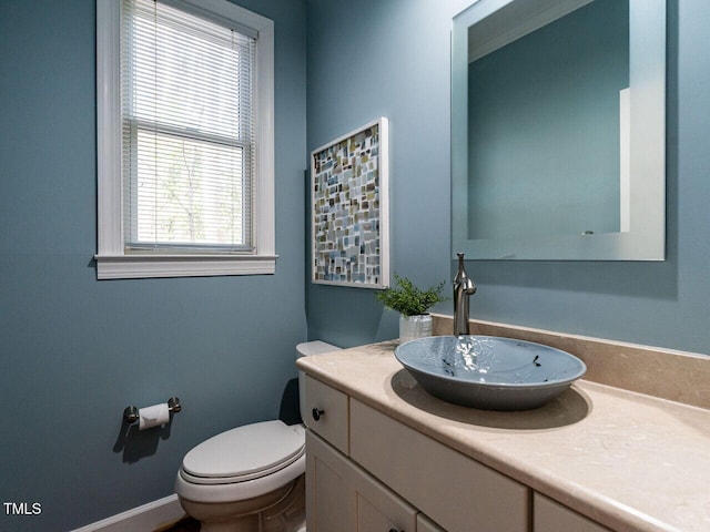 half bathroom with baseboards, toilet, and vanity