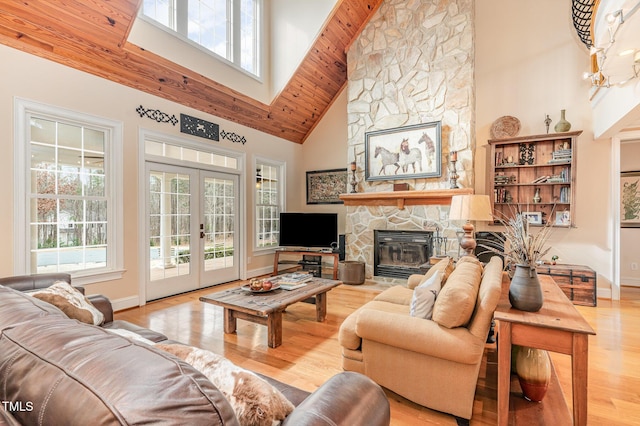 living area with baseboards, a stone fireplace, french doors, a high ceiling, and wood finished floors