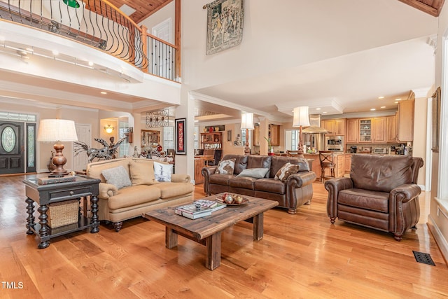 living area with light wood-type flooring, a high ceiling, visible vents, and ornamental molding