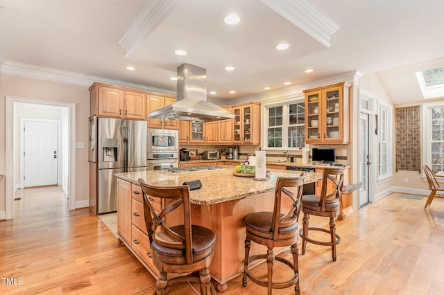 kitchen with a center island, light stone countertops, ornamental molding, appliances with stainless steel finishes, and island exhaust hood