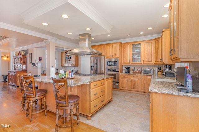 kitchen featuring island exhaust hood, light stone counters, a kitchen breakfast bar, backsplash, and stainless steel appliances