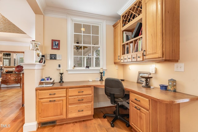 office space with built in desk, light wood-type flooring, crown molding, and visible vents