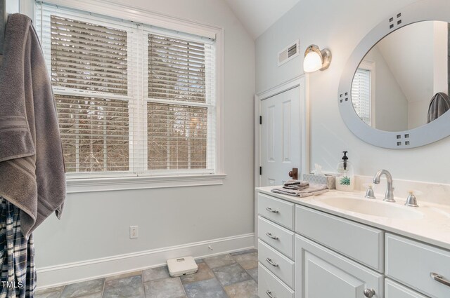 bathroom featuring vanity, baseboards, visible vents, lofted ceiling, and stone finish floor