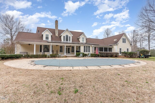 rear view of house featuring a patio, a covered pool, a chimney, ceiling fan, and a lawn