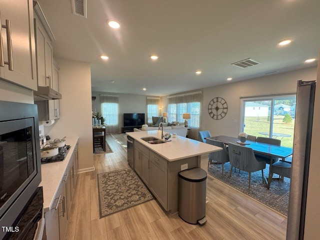 kitchen featuring visible vents, light wood-type flooring, a sink, under cabinet range hood, and stainless steel appliances