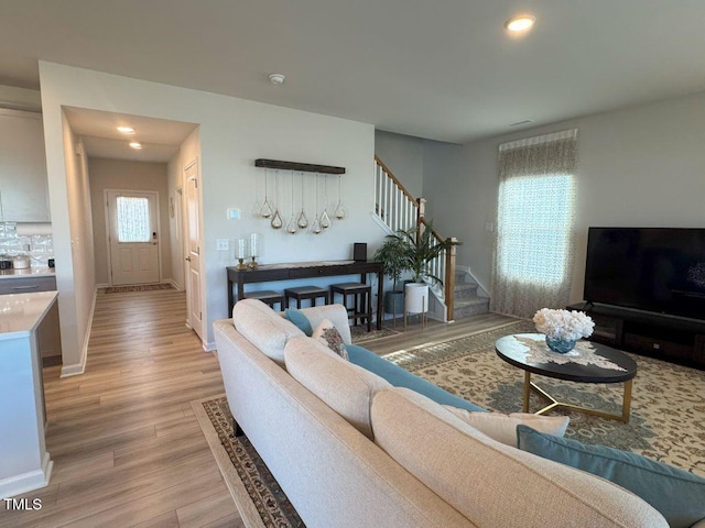 living area featuring stairway, recessed lighting, baseboards, and light wood finished floors