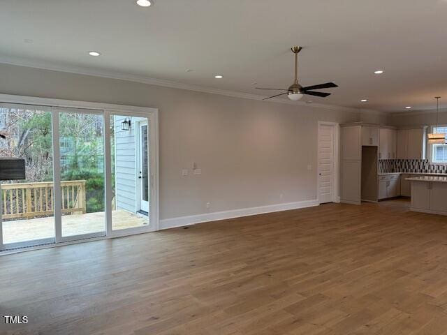 unfurnished living room featuring light wood-type flooring, baseboards, ornamental molding, and a ceiling fan