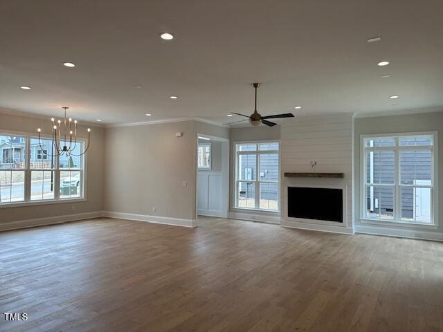 unfurnished living room featuring ceiling fan with notable chandelier, crown molding, a healthy amount of sunlight, and wood finished floors