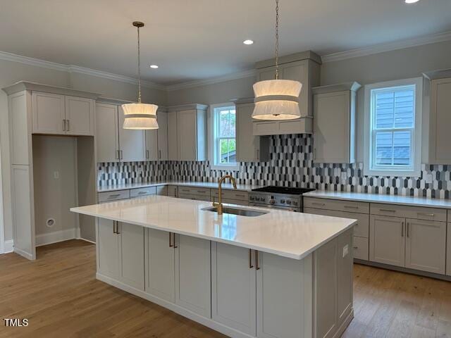 kitchen with a center island with sink, high end stainless steel range, a sink, light wood-style floors, and light countertops