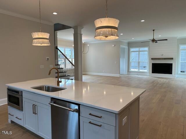 kitchen featuring light wood finished floors, ornamental molding, stainless steel dishwasher, a ceiling fan, and a sink