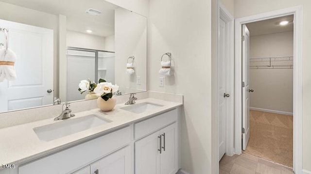 bathroom with a walk in closet, double vanity, walk in shower, and a sink