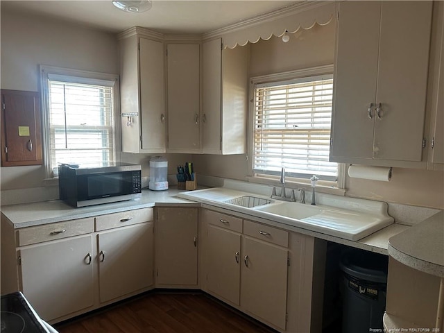 kitchen with stainless steel microwave, dark wood-type flooring, light countertops, white cabinets, and a sink