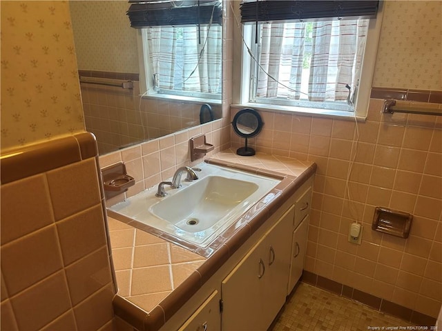 bathroom featuring wallpapered walls, tile walls, vanity, and wainscoting